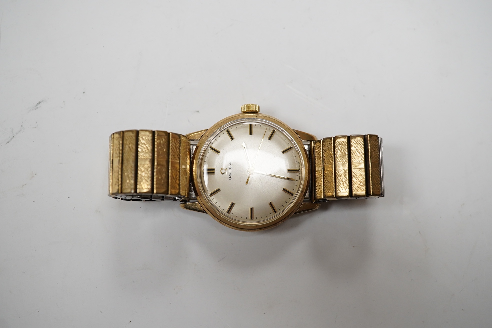 A gentleman's yellow metal Omega manual wind wrist watch, with baton numerals, case diameter 34mm, on an associated rolled gold flexible strap. Condition - fair